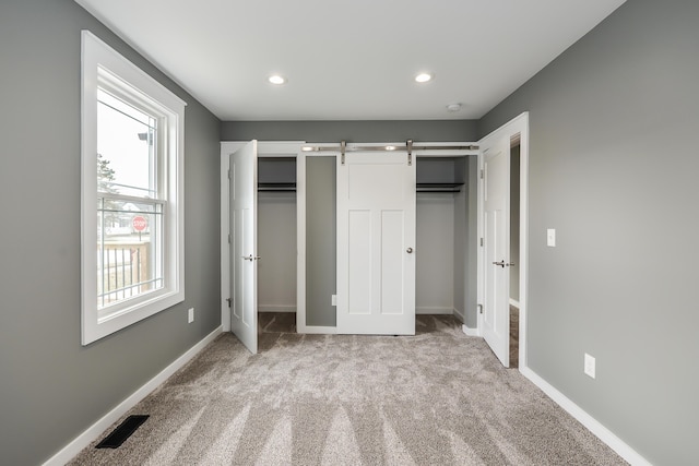 unfurnished bedroom with a barn door and light colored carpet