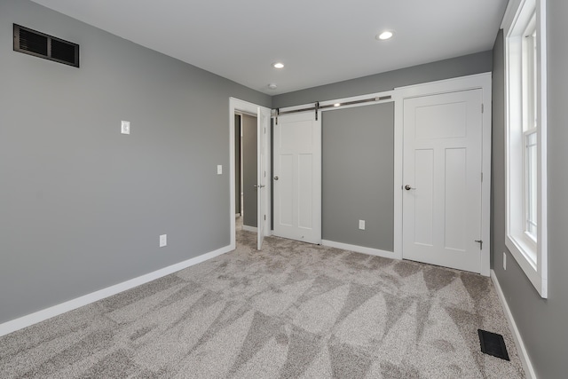 unfurnished bedroom featuring a barn door and light carpet