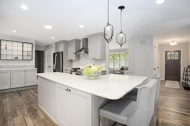 kitchen with wall chimney range hood, dark wood-type flooring, stainless steel appliances, and a center island