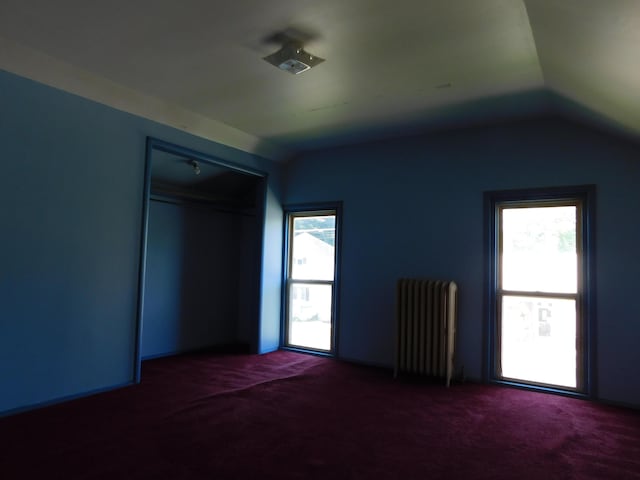 carpeted empty room with radiator heating unit and vaulted ceiling