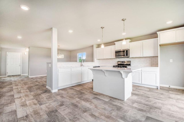 kitchen with appliances with stainless steel finishes, a kitchen island, light hardwood / wood-style flooring, white cabinetry, and hanging light fixtures