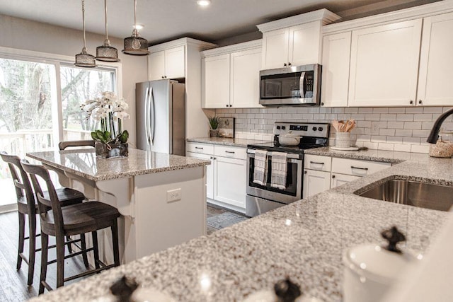 kitchen with white cabinets, hanging light fixtures, decorative backsplash, light stone counters, and stainless steel appliances