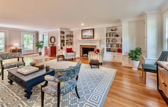 living room featuring crown molding, built in features, a fireplace, and light hardwood / wood-style flooring