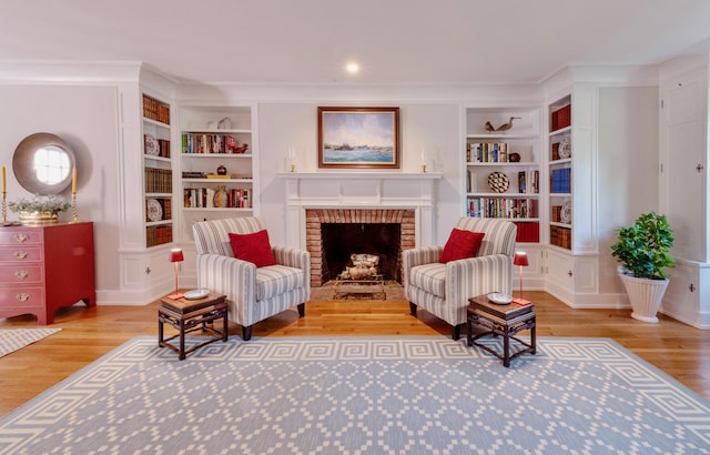 living area with built in shelves, a brick fireplace, ornamental molding, and hardwood / wood-style floors