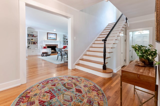 stairs featuring built in shelves, hardwood / wood-style flooring, crown molding, and a brick fireplace