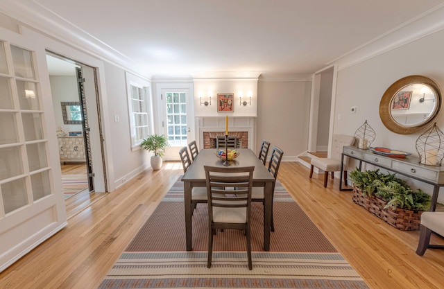 dining space with a brick fireplace, light hardwood / wood-style flooring, and ornamental molding