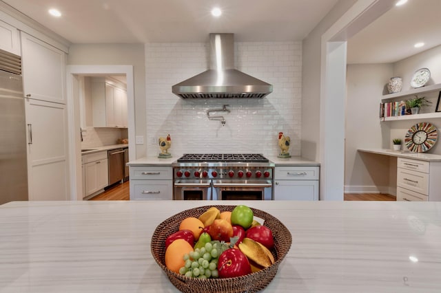 kitchen with high quality appliances, decorative backsplash, white cabinets, and wall chimney exhaust hood