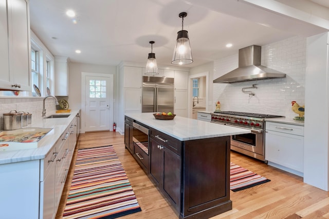 kitchen featuring built in appliances, sink, white cabinets, and wall chimney range hood