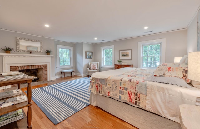 bedroom featuring a fireplace, ornamental molding, and light wood-type flooring