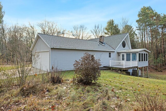 exterior space featuring a sunroom, a garage, a wooden deck, and a lawn