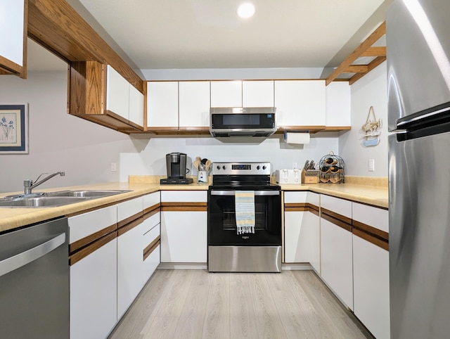 kitchen with sink, white cabinets, stainless steel appliances, and light hardwood / wood-style flooring