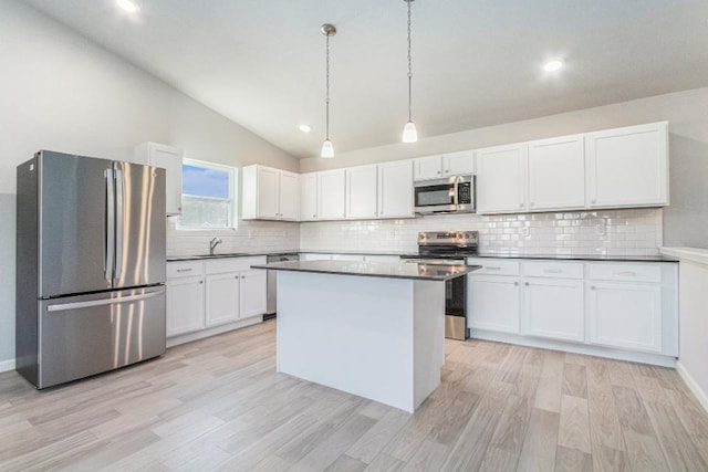 kitchen with lofted ceiling, sink, appliances with stainless steel finishes, white cabinetry, and hanging light fixtures