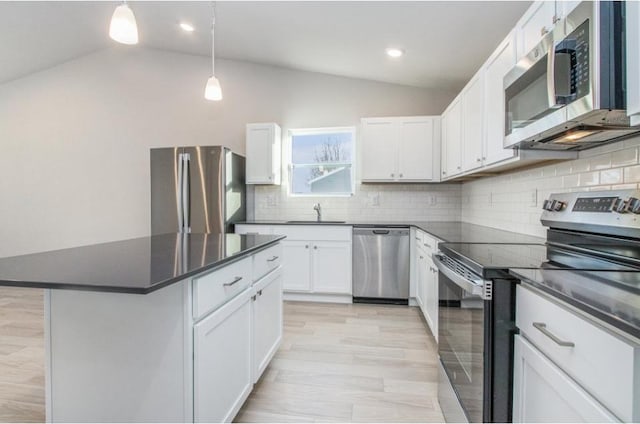 kitchen with vaulted ceiling, decorative light fixtures, white cabinets, a center island, and stainless steel appliances