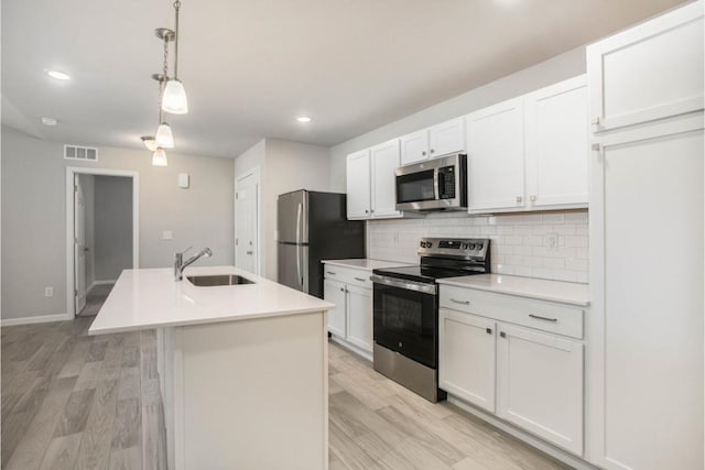 kitchen with sink, hanging light fixtures, stainless steel appliances, a center island with sink, and white cabinets