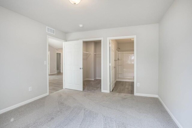 unfurnished bedroom with light carpet, ensuite bathroom, a spacious closet, and a closet