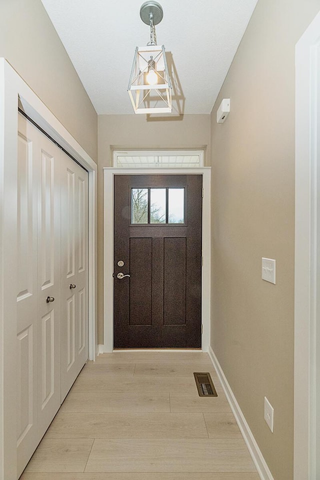 doorway to outside with light wood-type flooring and an inviting chandelier