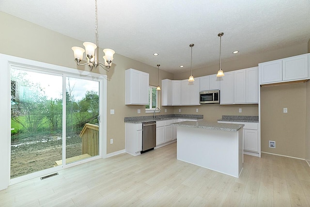 kitchen with sink, stainless steel appliances, white cabinets, a kitchen island, and decorative light fixtures