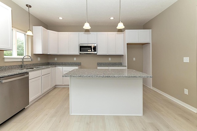 kitchen featuring a kitchen island, appliances with stainless steel finishes, white cabinetry, hanging light fixtures, and light stone countertops