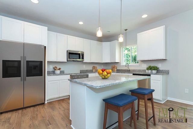 kitchen featuring a kitchen island, pendant lighting, white cabinets, light stone counters, and stainless steel appliances