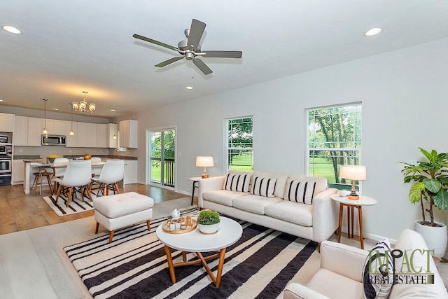 living room featuring ceiling fan with notable chandelier, a healthy amount of sunlight, and light hardwood / wood-style floors