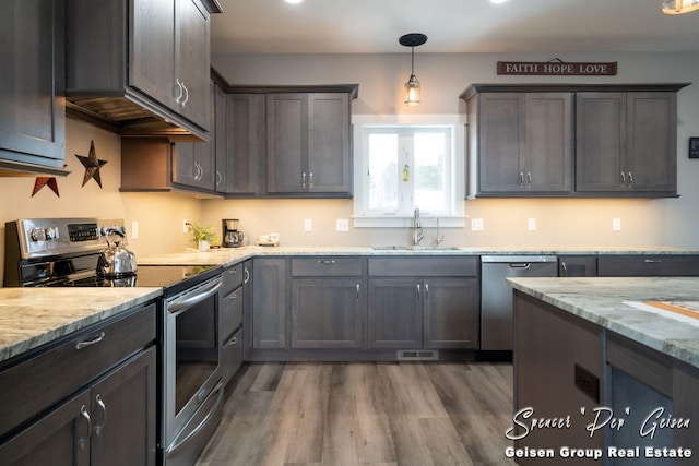 kitchen with light stone countertops, stainless steel appliances, sink, pendant lighting, and dark hardwood / wood-style floors