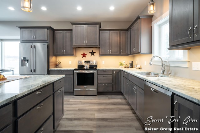 kitchen with light wood-type flooring, dark brown cabinetry, stainless steel appliances, sink, and pendant lighting