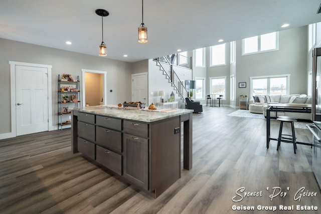 kitchen featuring light stone countertops, a center island, dark hardwood / wood-style floors, pendant lighting, and dark brown cabinets