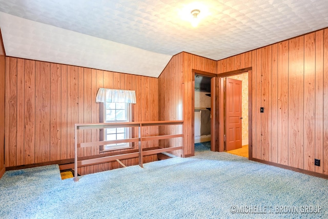 unfurnished room with carpet floors, wooden walls, a textured ceiling, and lofted ceiling