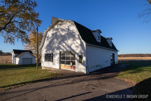 view of side of home with a garage, a rural view, an outbuilding, and a lawn