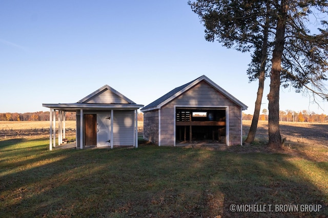 back of property with a yard, a rural view, and an outdoor structure