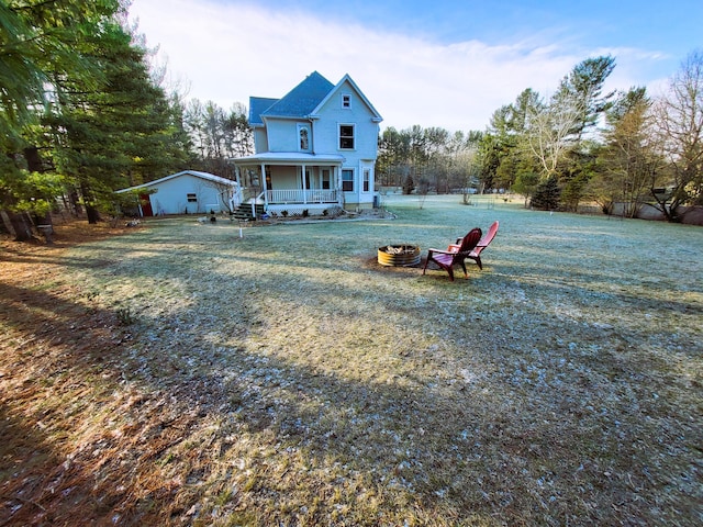 rear view of property featuring a lawn, a fire pit, and covered porch