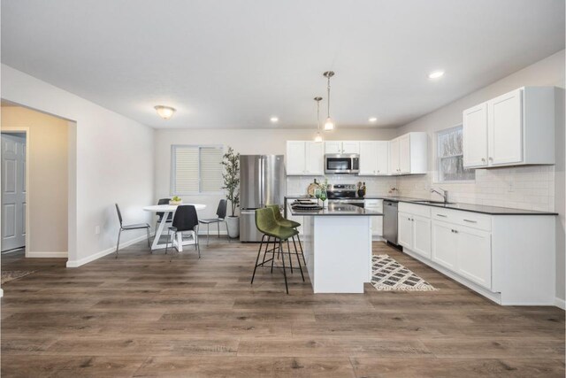 kitchen with decorative light fixtures, white cabinets, a kitchen breakfast bar, a center island, and stainless steel appliances