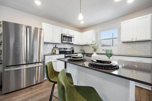 kitchen with appliances with stainless steel finishes, decorative light fixtures, wood-type flooring, white cabinets, and a kitchen breakfast bar