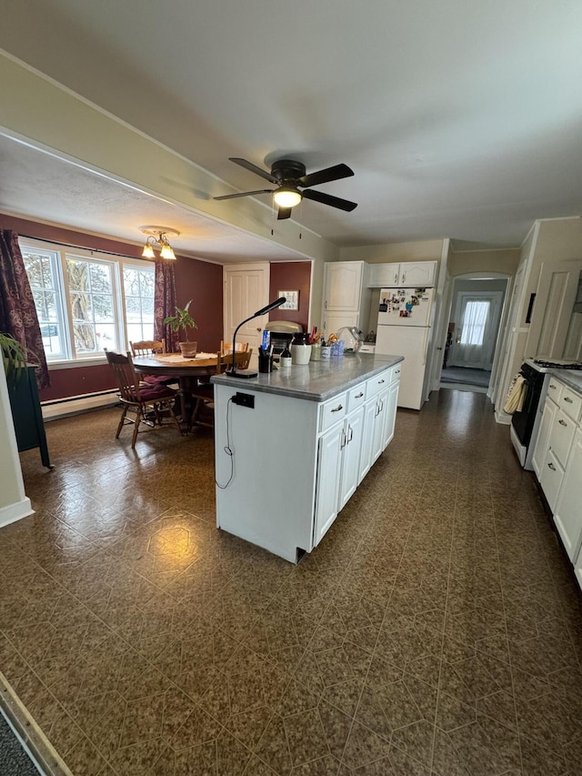 kitchen featuring white appliances, a kitchen island with sink, a baseboard heating unit, white cabinets, and ceiling fan