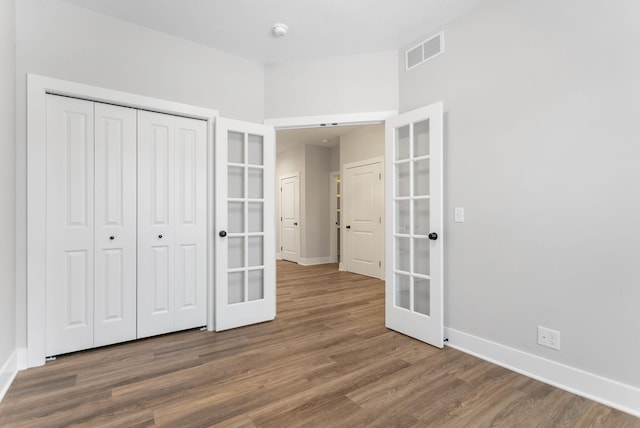 unfurnished bedroom with french doors, a closet, and wood-type flooring