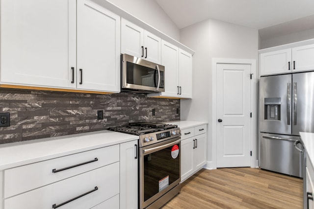 kitchen featuring white cabinetry, stainless steel appliances, tasteful backsplash, vaulted ceiling, and light wood-type flooring