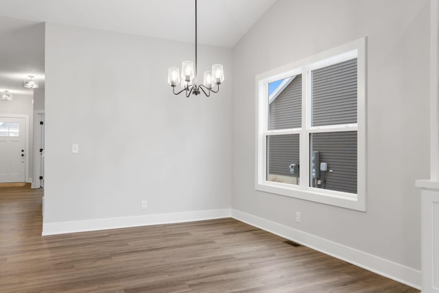 unfurnished dining area featuring hardwood / wood-style floors, a notable chandelier, and vaulted ceiling