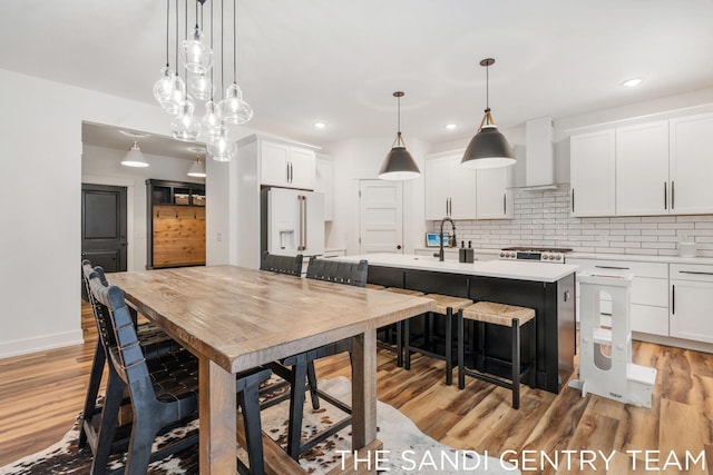 kitchen featuring pendant lighting, wall chimney exhaust hood, white cabinetry, and a kitchen island with sink