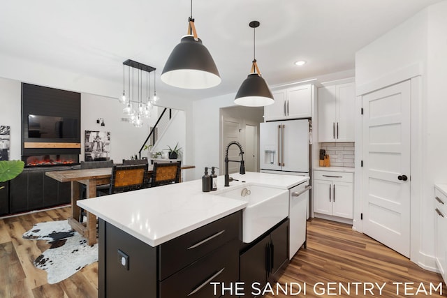 kitchen with white cabinets, decorative light fixtures, a large fireplace, and an island with sink