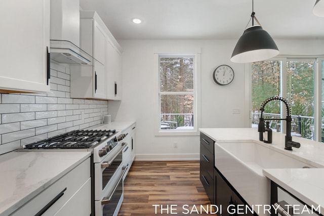 kitchen featuring gas range, white cabinets, wall chimney exhaust hood, and decorative light fixtures