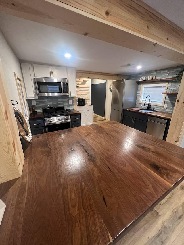 kitchen featuring backsplash, stainless steel appliances, wooden walls, sink, and white cabinets