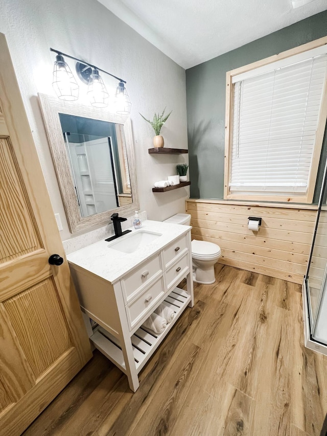 bathroom with vanity, wooden walls, hardwood / wood-style flooring, toilet, and walk in shower