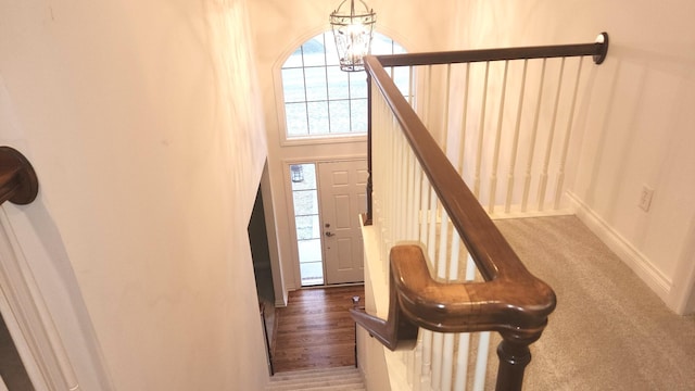 stairway with carpet floors and an inviting chandelier