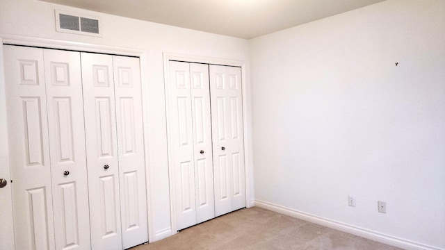 unfurnished bedroom with light carpet and multiple closets