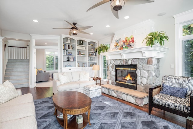 living room featuring built in features, a fireplace, ceiling fan, and dark hardwood / wood-style floors