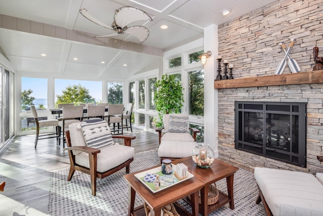 sunroom / solarium featuring a stone fireplace, ceiling fan, and coffered ceiling