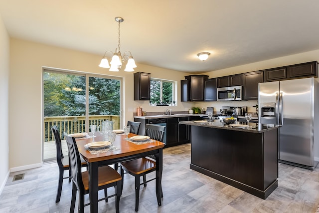 kitchen featuring dark brown cabinets, stainless steel appliances, a notable chandelier, a kitchen island, and decorative light fixtures