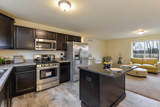 kitchen featuring dark brown cabinetry, stainless steel appliances, a kitchen island, and light wood-type flooring