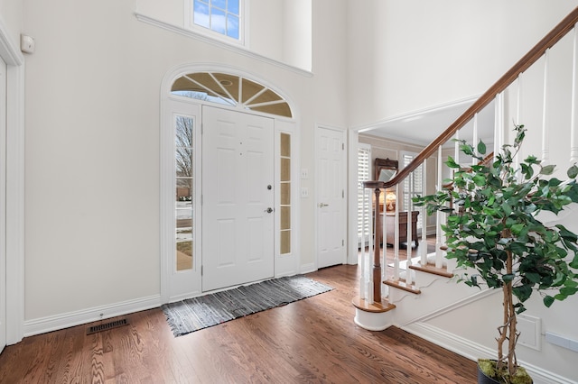 entrance foyer featuring a towering ceiling, stairway, wood finished floors, and visible vents