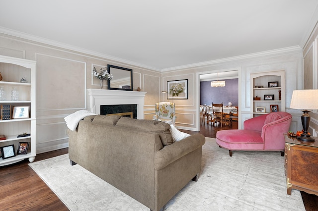 living area featuring a decorative wall, wood finished floors, a high end fireplace, built in features, and crown molding